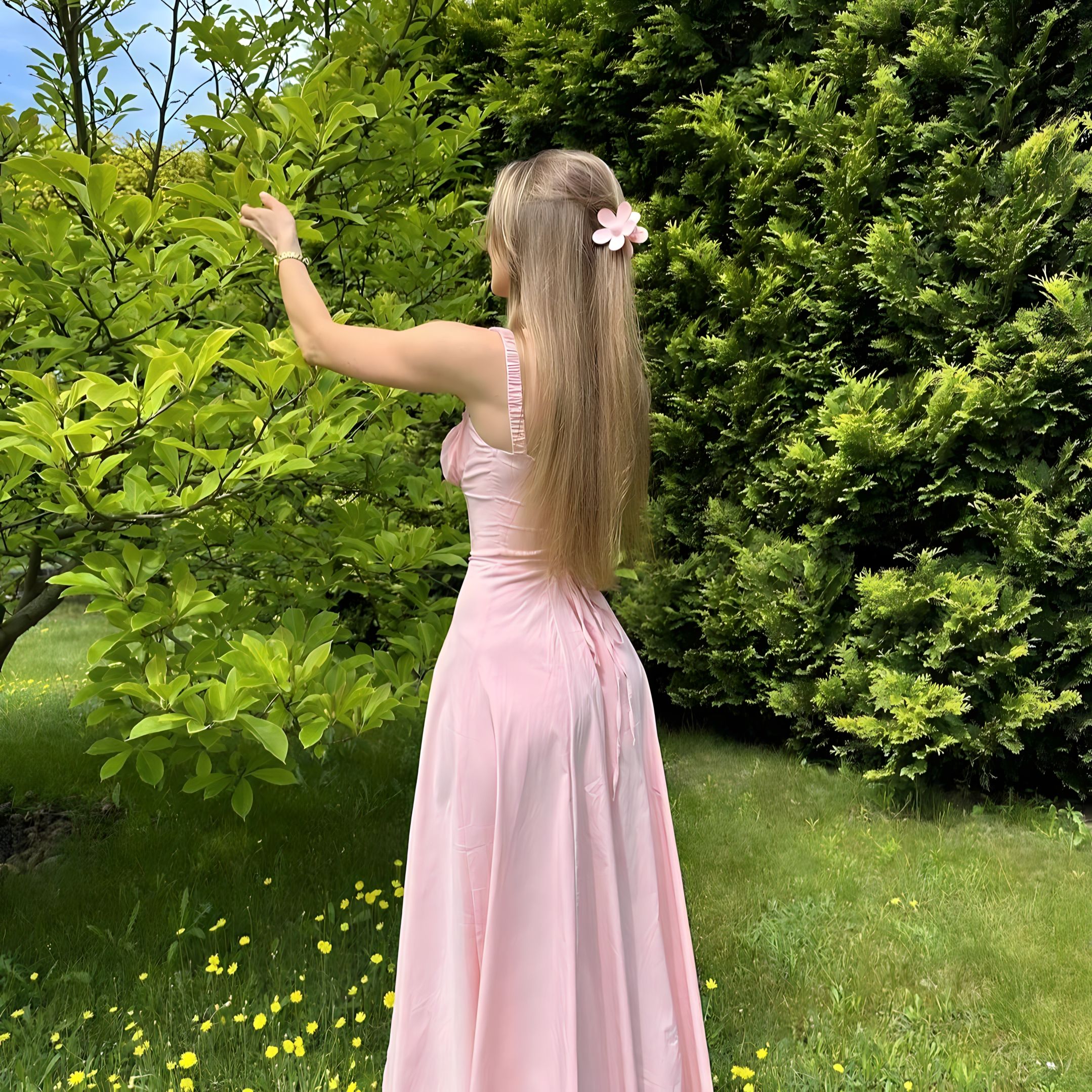 Woman in a long pink dress seen from behind in a garden