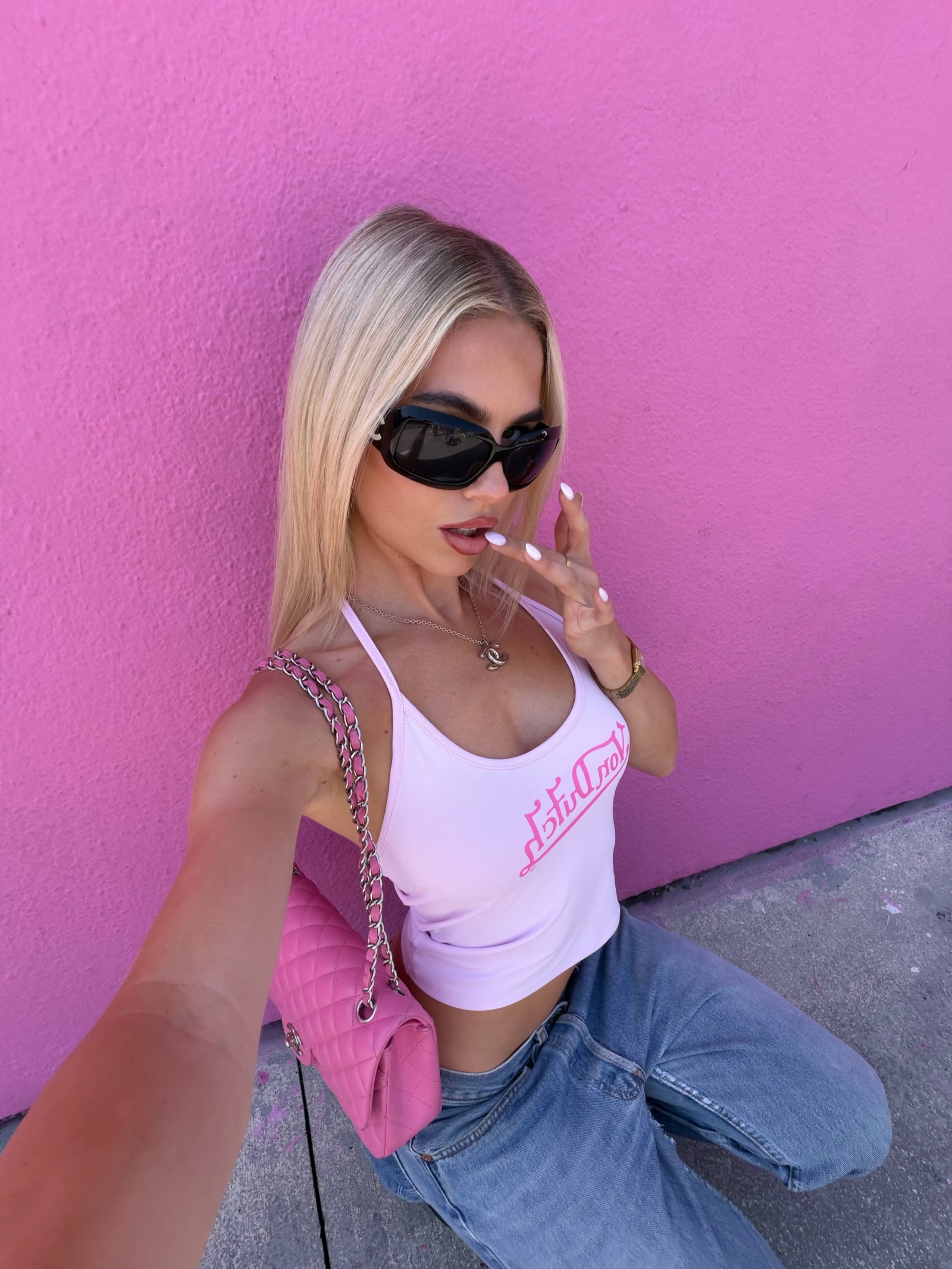Woman in sunglasses taking a selfie against a bright pink wall