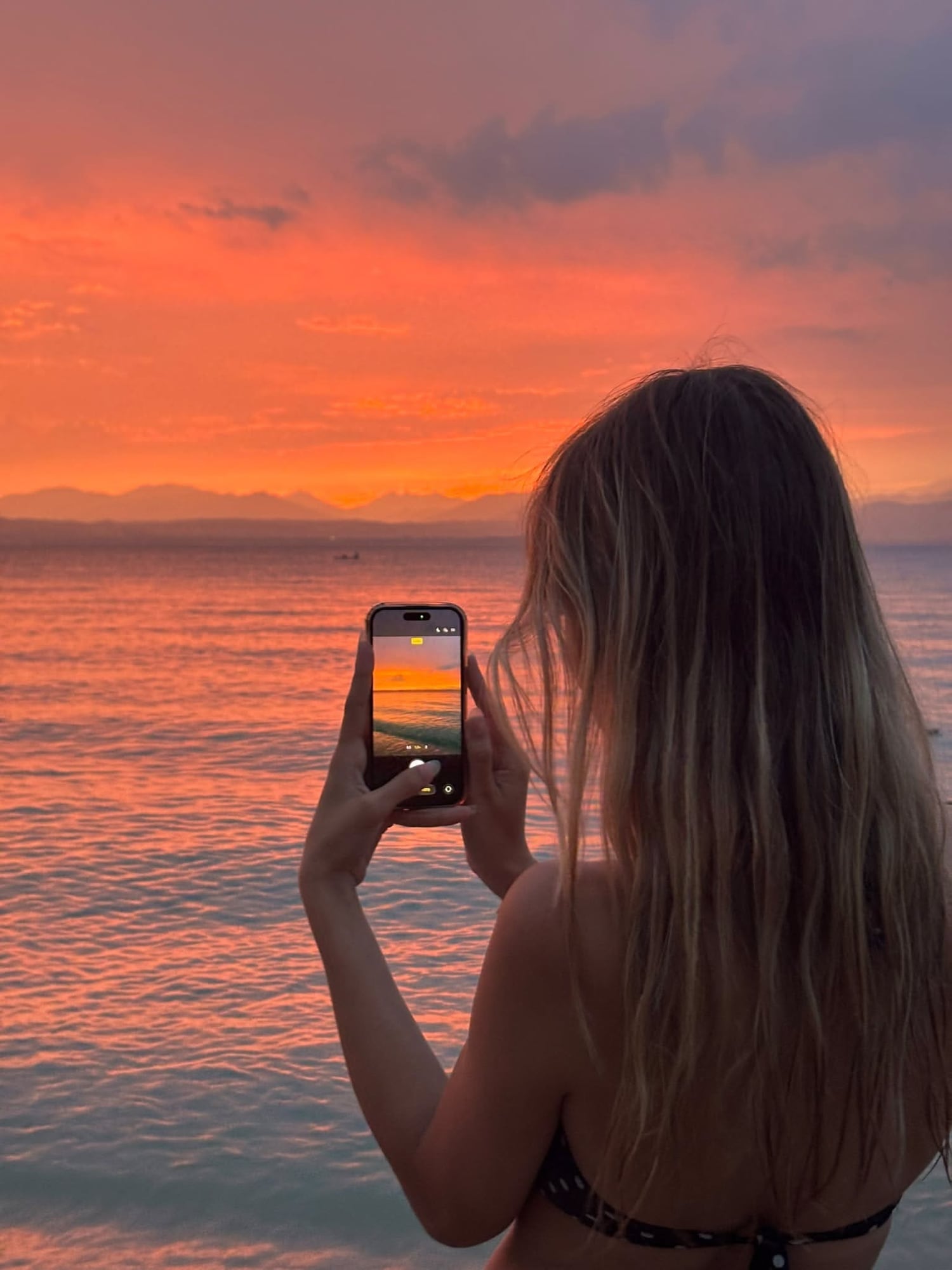 Woman filming the sunset over the sea on her phone