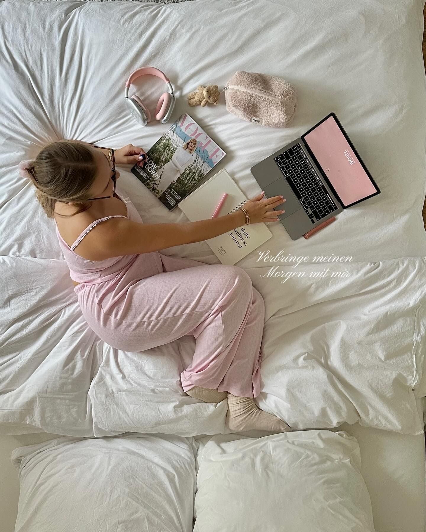 Woman in pink pyjamas working on a laptop on her bed