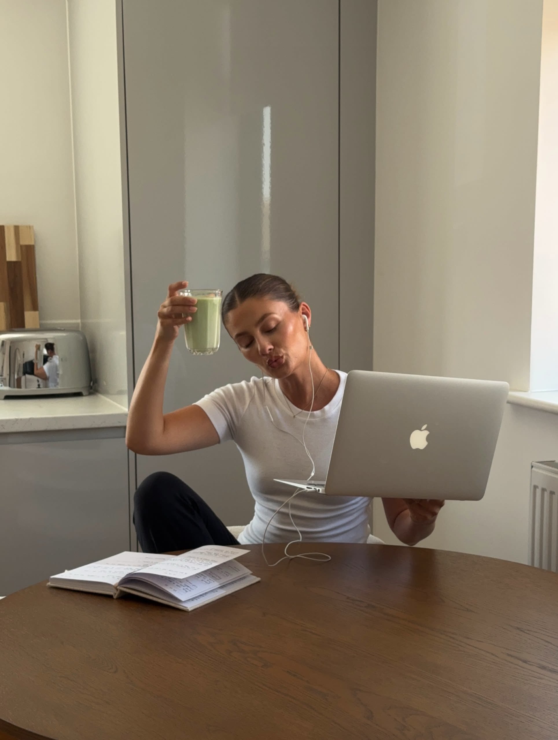 Woman at a kitchen table with her laptop and a drink