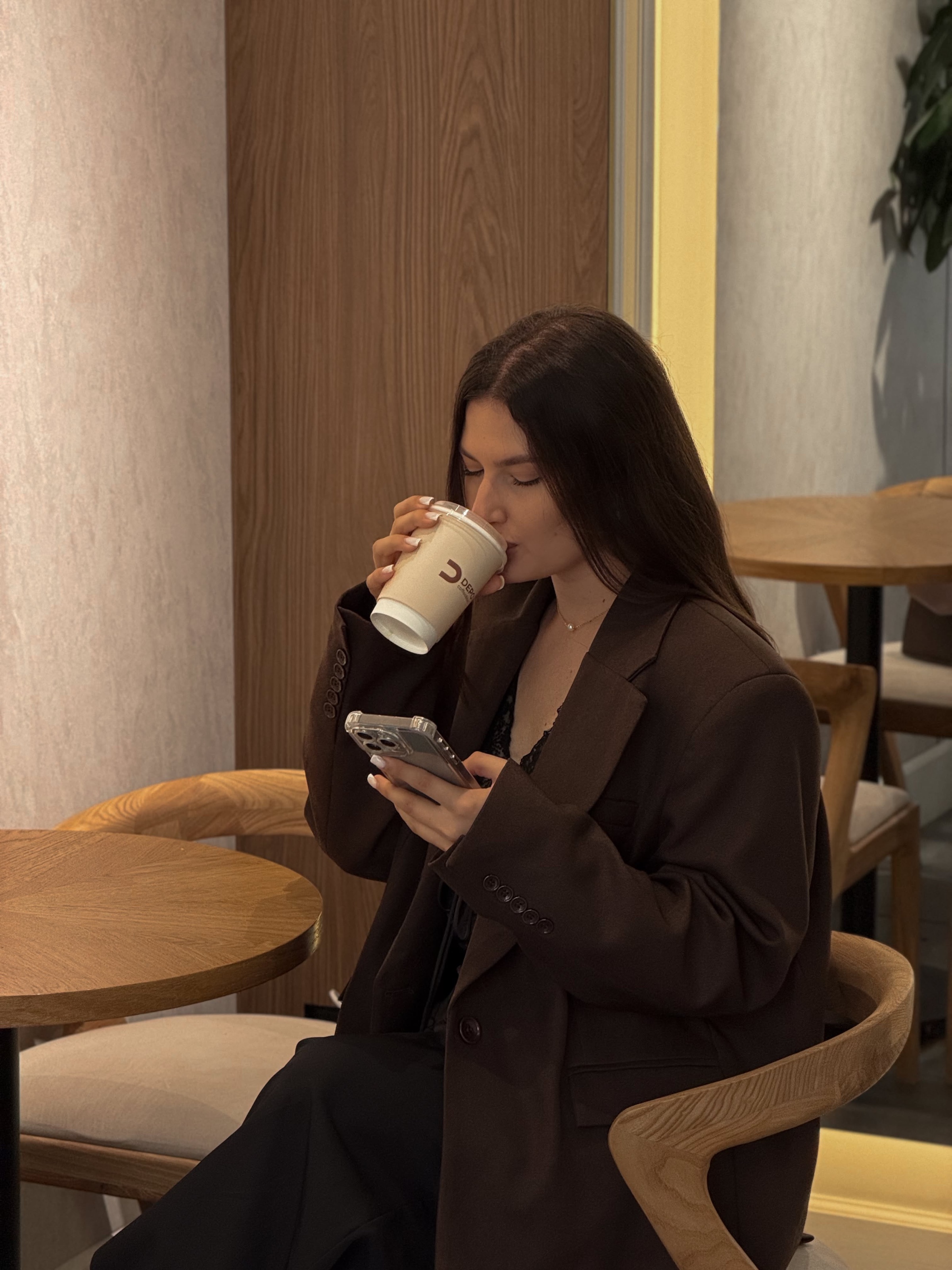 Woman in a café sipping coffee while checking her phone