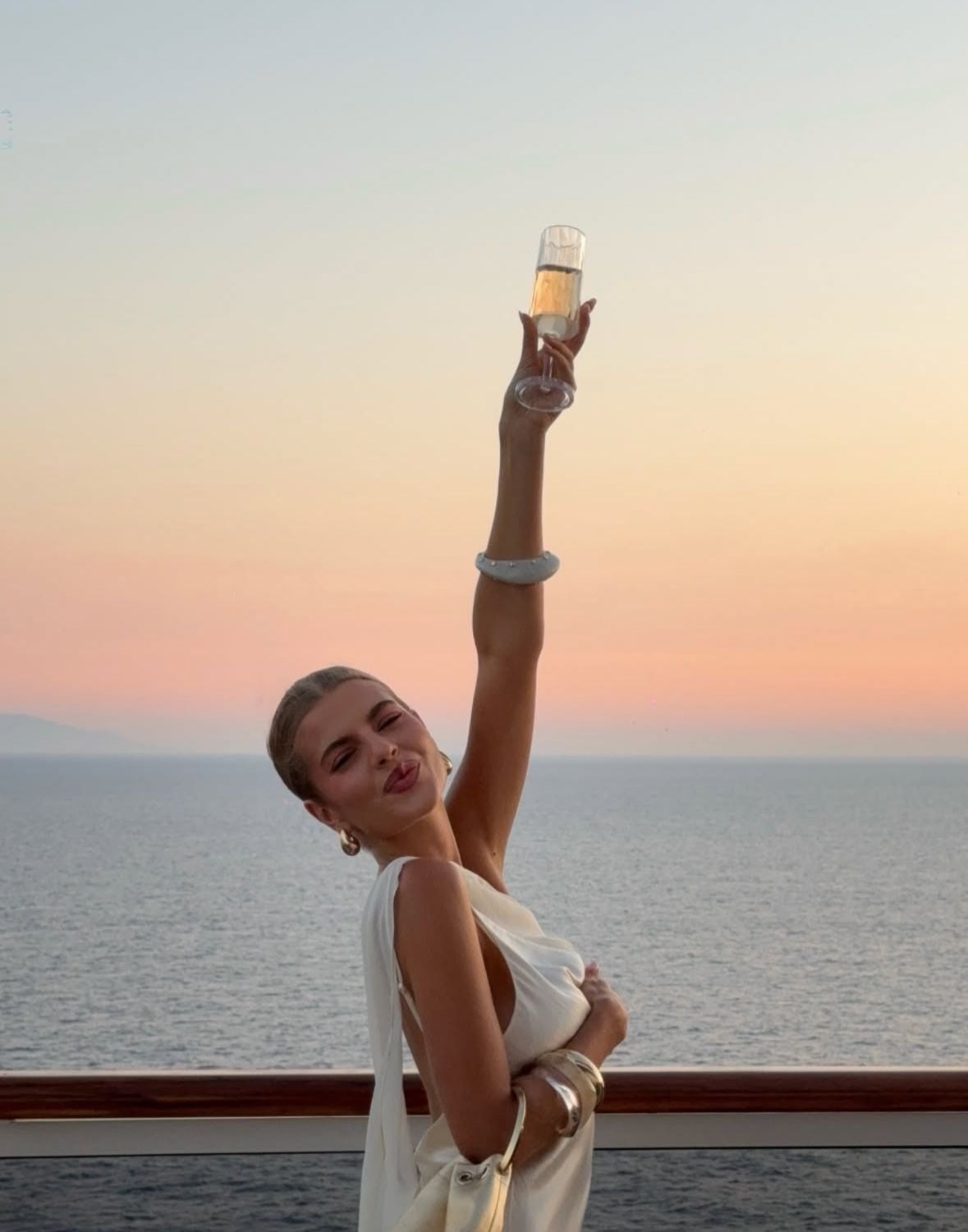 Woman raising a glass to the sunset over the sea