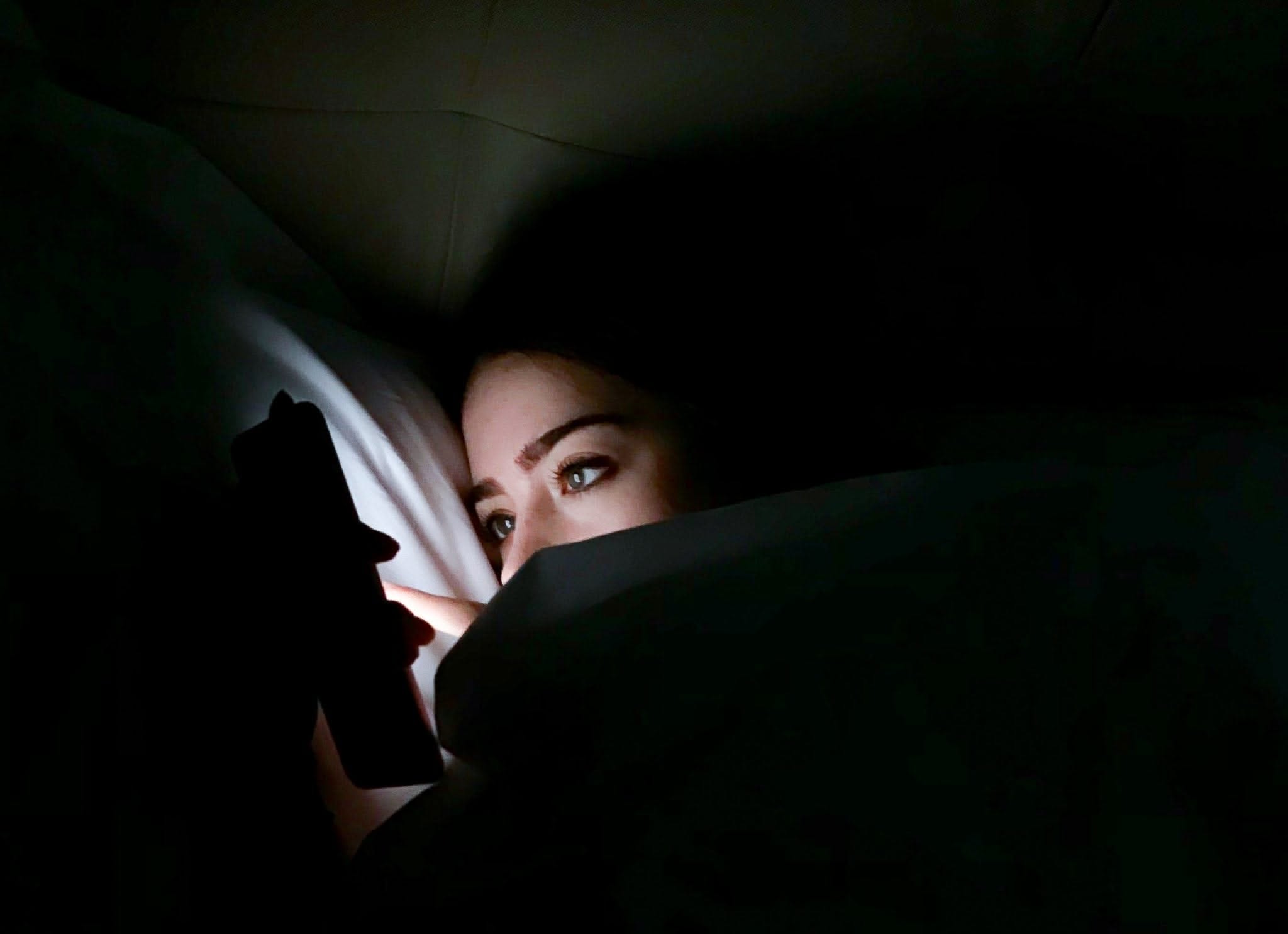 Woman's face lit by her phone in a dark room